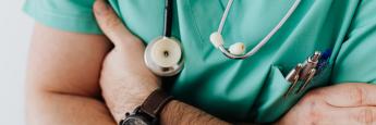 Man in green scrubs wearing a watch and crossing his arms also with a stethoscope around his neck