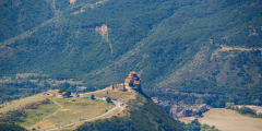 a photo of a castle on a hill nestled in between mountains covered in green trees