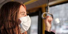 a photo of a brunette women standing on the bus wearing a white surgical mask 