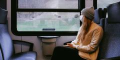 Woman wearing a mask sitting on a train and looking out the window