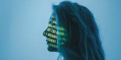 Side profile of a woman against a blue backdrop with binary code lit up across her face