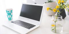 Laptop on a white counter with yellow flowers in a glass next to it and a blue glass