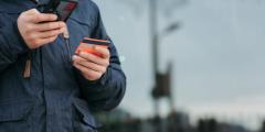 Person in a blue jacket holding a phone and a red credit card set against a blurry background