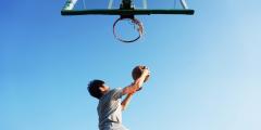 Low angle shot of a person with a basketball going for a layup on a basketball hoop against a light blue sky
