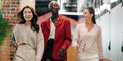 Three women in an office walking side by side while smiling
