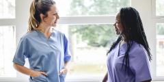 Two women in blue and purple scrubs talking to each other in a hospital