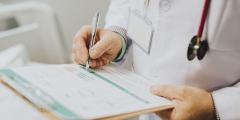 Doctor in a white coat holding a clipboard with a stethoscope and writing something